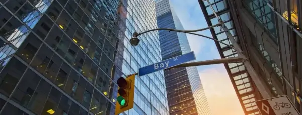 A green traffic light and Bay Street sign are mounted on a pole, surrounded by tall glass office buildings reflecting the sky at sunset—a cityscape where salary benchmarking shapes fair employee benefits.