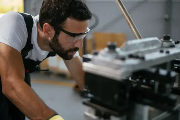 A man wearing safety glasses and work clothes closely inspects or operates industrial machinery—showcasing the hands-on skills valued in Ontario manufacturing jobs projected to be in-demand by 2026.